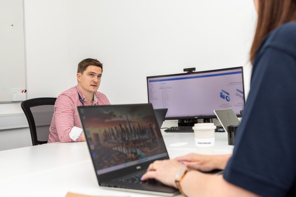 Two members of CloudTech24 sit opposite each other working at their laptops